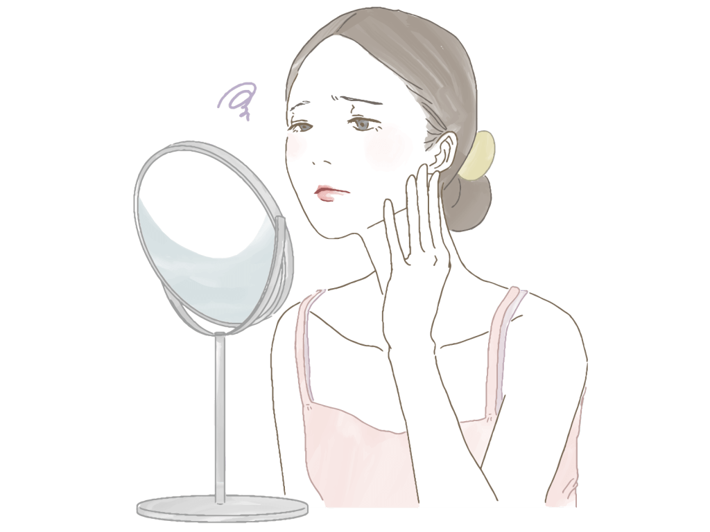 鏡の前で自分の顔を見ている女性。彼女は疲れた表情をしており、頬に手を添えている。